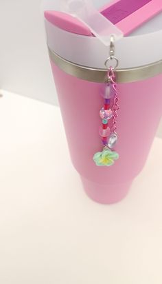 a pink cup with some charms hanging from it's side on a white table