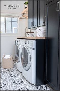 a washer and dryer in a small laundry room with black cabinets, white tile flooring and wood shelves