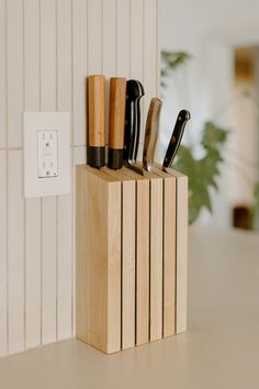 a wooden block holding knives and other kitchen utensils in front of a white wall