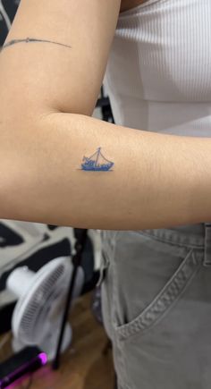 a woman's arm with a small blue boat tattoo on the left arm and right arm