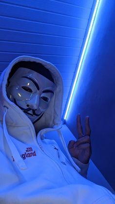 a person wearing a white mask and hoodie making the v for vender sign