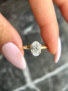 a woman's hand holding a ring with a diamond on it and the middle finger