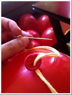 a hand holding a pair of scissors over a red object with yellow string on it