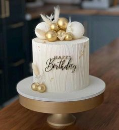 a white and gold birthday cake sitting on top of a wooden table