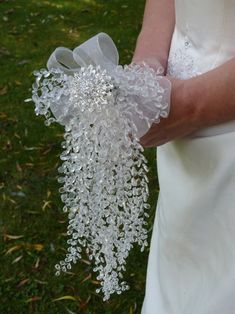 a person in a wedding dress holding a bouquet of white flowers and ribbons on their arm