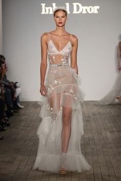 a model walks the runway in a white dress with sheer fabric and flowers on it