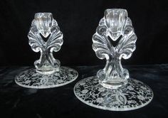 two glass candlesticks sitting on top of a black cloth covered table with an ornate design