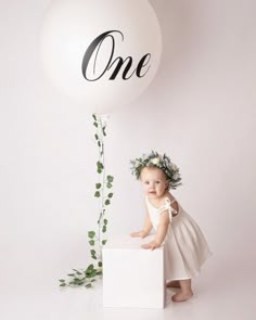 a baby girl standing in front of a balloon with the word one written on it