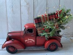 an old red truck with a christmas tree in the back and plaid blanket on top