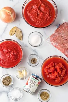 ingredients to make tomato sauce laid out on a marble counter top, including tomatoes, garlic and seasonings