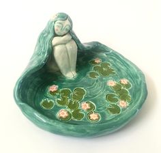 a ceramic figurine sitting on top of a green bowl filled with water lilies