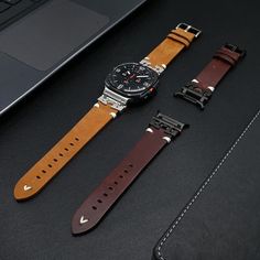 two watches sitting next to each other on top of a black table near a laptop