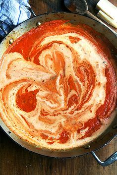 a skillet filled with sauce and cheese on top of a wooden table next to utensils