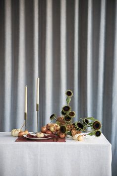 a table with sunflowers, onions and candles on it in front of a curtain