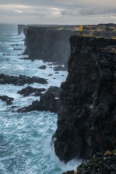 a person standing on the edge of a cliff overlooking the ocean with waves crashing against it