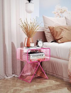 a pink side table with books and a clock on it in front of a bed