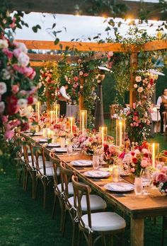 a long table is set with flowers and candles for an outdoor wedding reception in the evening