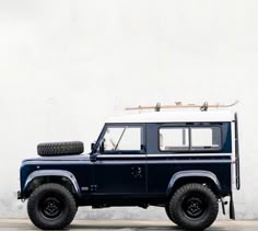 a blue land rover is parked in front of a white wall with a snowboard on top