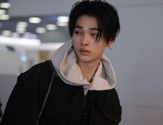 a young man with black hair wearing a jacket and holding a handbag in front of him