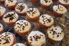 cupcakes with white frosting and black sprinkles are cooling on a rack