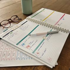 two notebooks, pen and eyeglasses on top of each other next to a cup