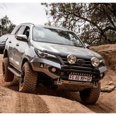 the front end of a silver toyota hilux driving down a dirt road with trees in the background