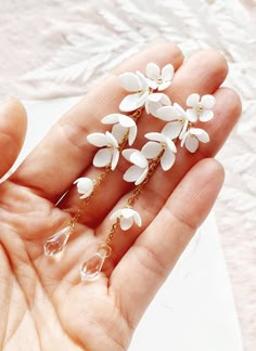 a person is holding some white flowers in their hand and wearing gold earrings