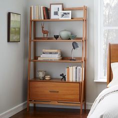 a bed room with a neatly made bed and a book shelf next to a window