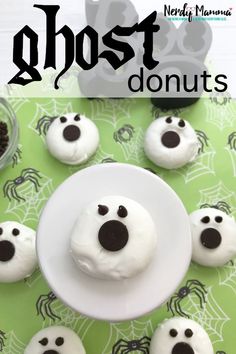 ghost donuts with white frosting and black eyes on a green tablecloth next to halloween decorations