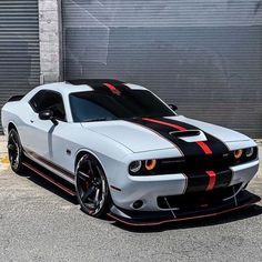 a white car with black and red stripes parked in front of a garage door on the street