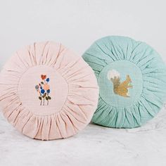 two decorative pillows sitting next to each other on a white counter top, one with a flower design and the other with a squirrel