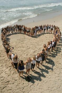 a group of people standing in the shape of a heart on top of a beach