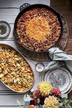 two large casserole dishes on a table with flowers and plates around the dish