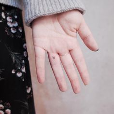 a person's hand with a tiny cross tattoo on their left thumb and the middle finger