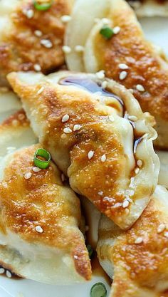 some dumplings are on a white plate with green onions and sesame seeds around them