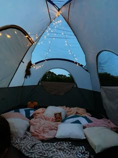 the inside of a tent with pillows and blankets on top of it, lights strung from the ceiling