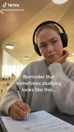 a woman sitting at a desk with headphones on and writing in a notepad