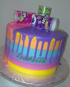 a birthday cake decorated with cans of sodas and rainbow icing on a silver platter