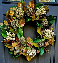 a wreath is hanging on a door with leaves and flowers in front of the doors