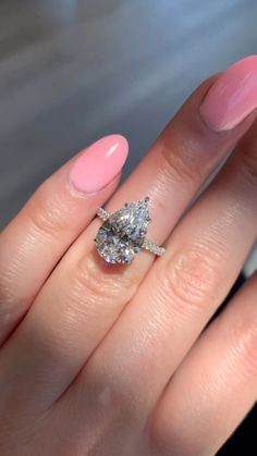 a woman's hand with pink manicured nails and an oval shaped diamond ring