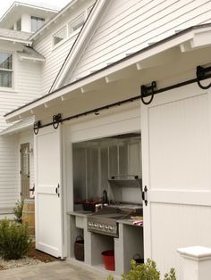 an outdoor kitchen is built into the side of a white house with black metal bars