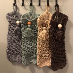 four crocheted bags hanging from hooks on the wall with tassels attached to them