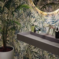 a bathroom with palm leaves on the wall and a plant next to the sink in front of it