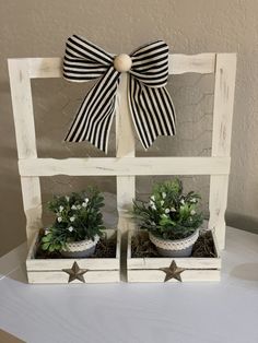 two white wooden boxes with plants in them and a bow on the top, sitting on a table