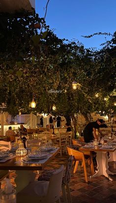 an outdoor dining area with tables and chairs at night, lit by hanging lights from the trees