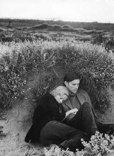 black and white photograph of man and woman sitting in the sand with wildflowers