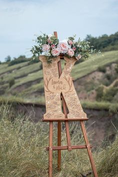 a wooden easel decorated with flowers and greenery on the side of a hill