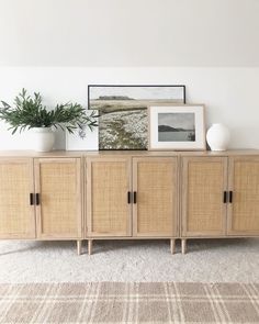 a sideboard with some plants on top of it and pictures above the drawers in front of it