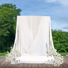 an outdoor ceremony setup with white flowers and draping on the back wall, surrounded by greenery