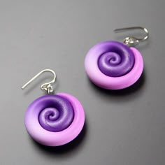 two pairs of earrings with purple and pink swirls on them sitting on a gray surface